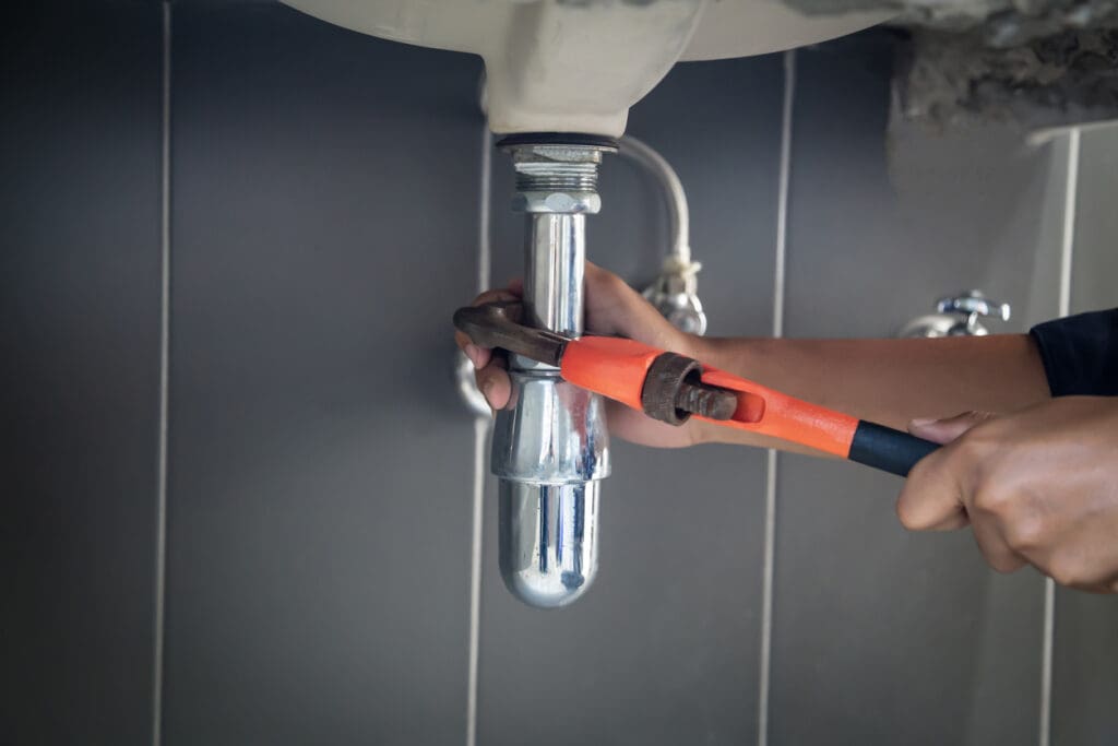 Plumber uses wrench to repair water pipe under sink There is maintenance to fix the water leak in the bathroom.with red wrench, plumbing install concept.